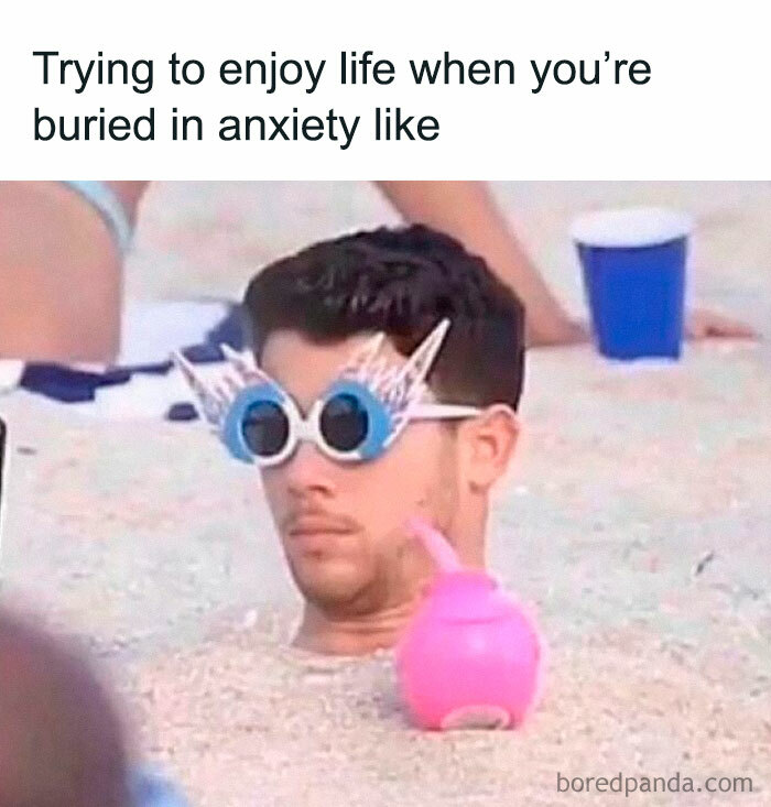 Man buried in sand wearing quirky glasses, sipping from a pink cup; perfect example of funny memes randomness.