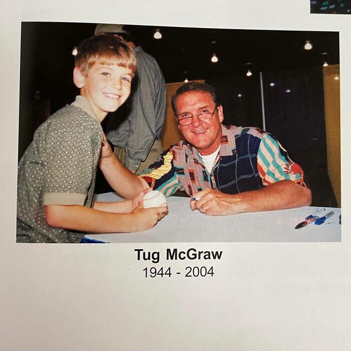 Young boy posing with a celebrity, holding a baseball, both smiling at an event with bright lighting.