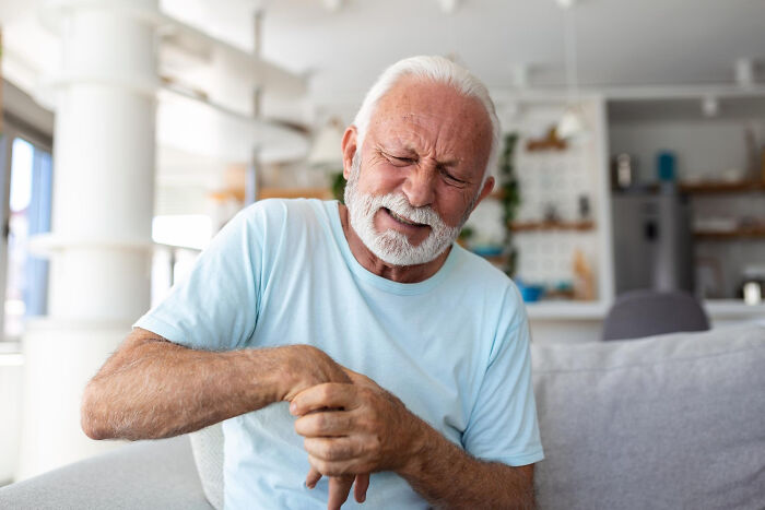 Elderly man wincing in pain while holding his hand, depicting harsh realities of aging.