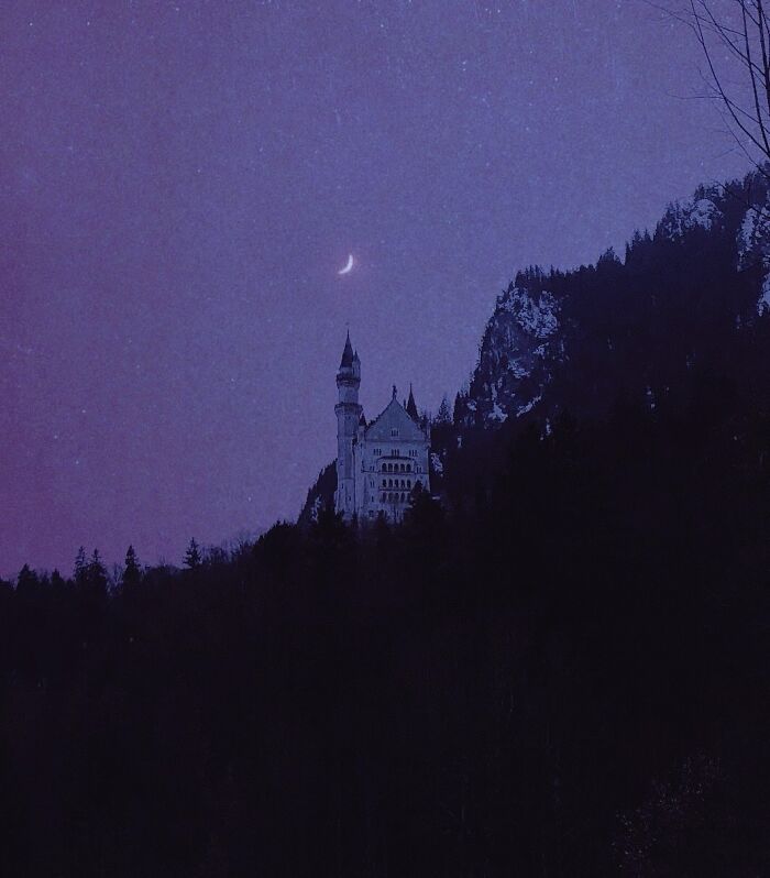 Dreamy dark escapism photography featuring a castle under a crescent moon against a purple night sky.
