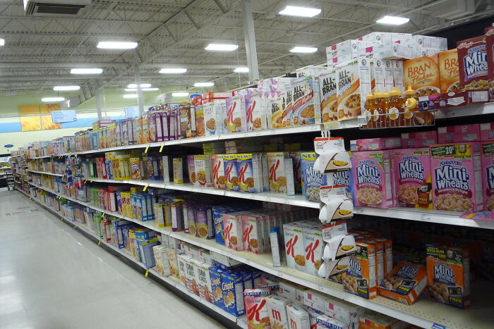 Grocery store aisle with shelves stocked with various restaurant food cereals and breakfast products in boxes and cartons.