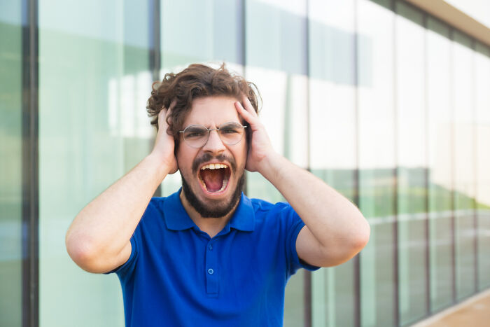 Man in a blue shirt and glasses looking scared outside near glass windows, illustrating the scariest things concept.