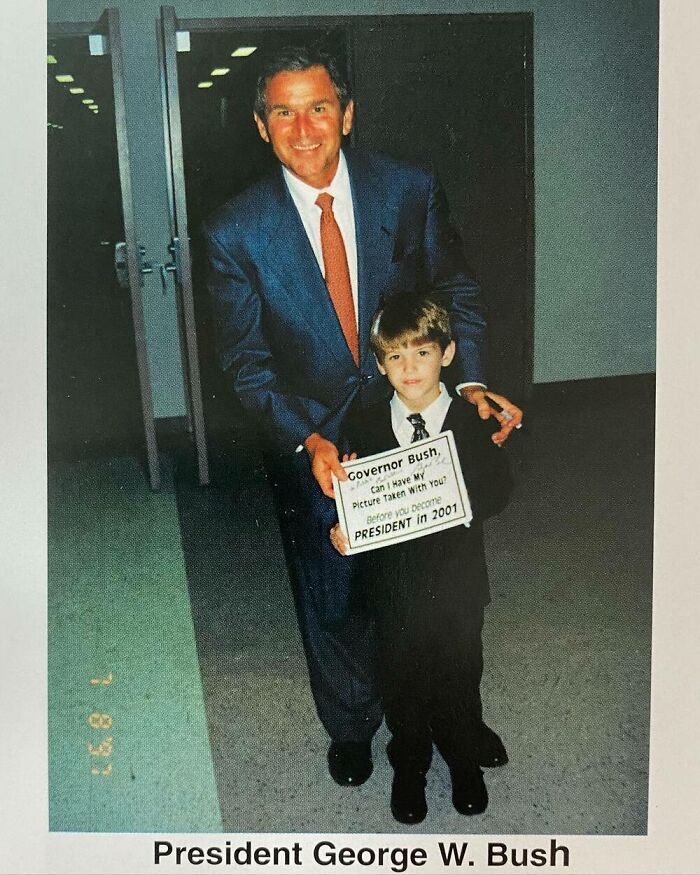 Young boy taking a photo with President George W. Bush, holding a sign, exemplifying childhood celebrity encounters.