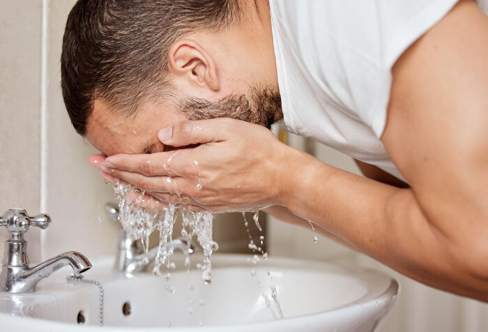 Man washing face at a sink, highlighting differences between men and women in daily routines.