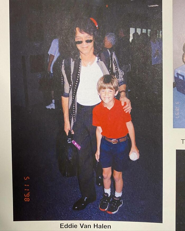 Boy posing with a celebrity, wearing a red shirt, shorts, and holding a ball, standing beside a person in sunglasses indoors.