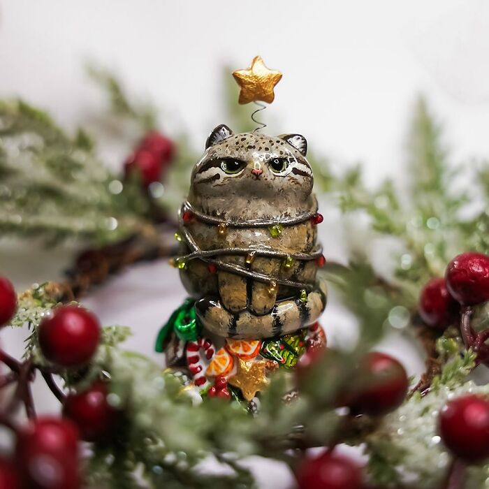 Adorable animal figurine by Vallavica, resembling a raccoon wrapped in festive lights, with greenery and berries in the background.