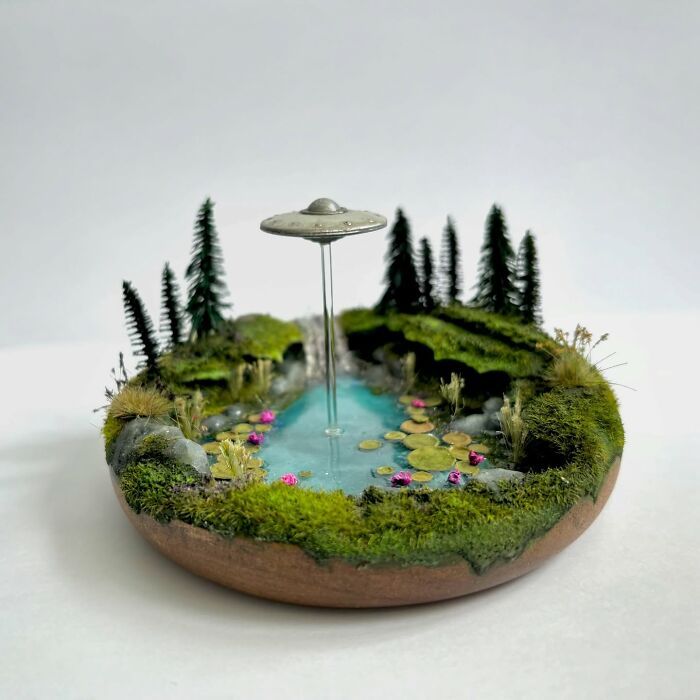 UFO-themed diorama with lush greenery, pond, and mysterious alien spacecraft hovering above.