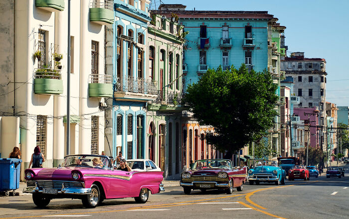Colorful city street with vibrant classic cars and pastel buildings, resembling a real-life painting.
