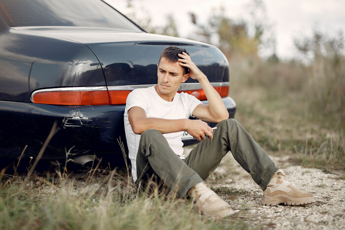 Man sitting by a car, looking thoughtful, symbolizes trusting gut instincts to avoid danger.