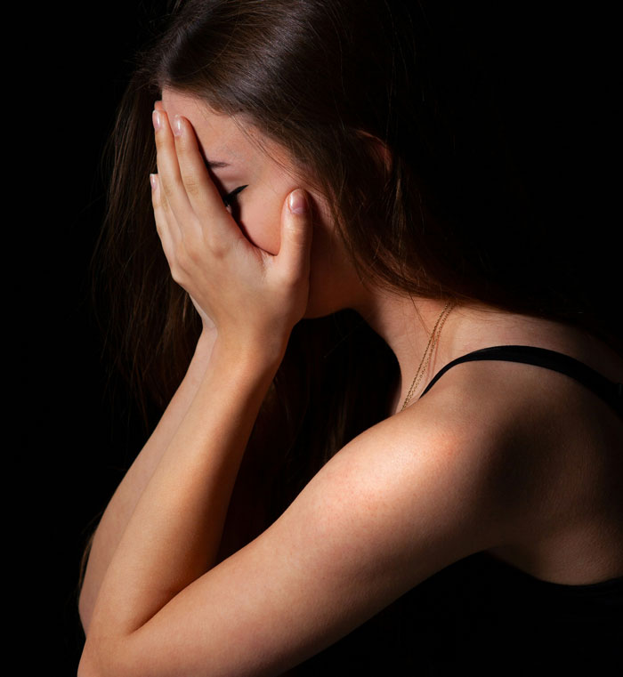 A woman covers her face in shock, reacting to unexpected family DNA results in a dimly lit room.