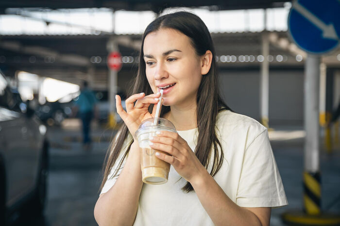 Woman drinking iced coffee in parking lot, illustrating everyday things that seem harmless but can be dangerous.