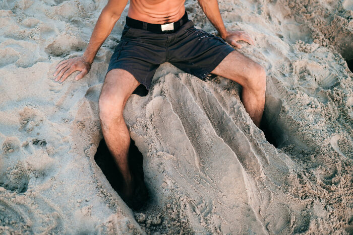 Man sitting on sand with legs buried, illustrating how everyday things can be dangerous.
