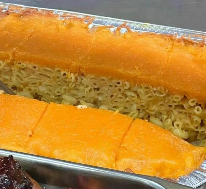 Unappetizing food photo showing a thick layer of orange cheese over dry macaroni in a foil tray.