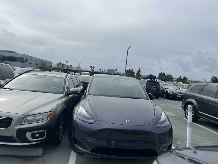 Tesla parked poorly, taking two spaces, illustrating lack of basic etiquette in a crowded parking lot.