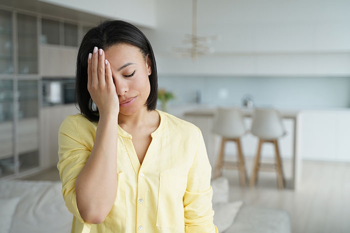 Woman in a yellow shirt looking frustrated in a modern living room.