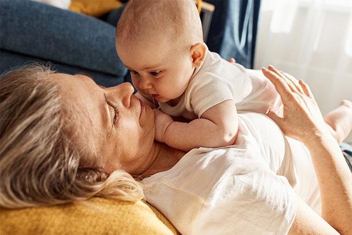 Grandmother and baby on couch, interacting closely, reflecting family boundaries and relationships.