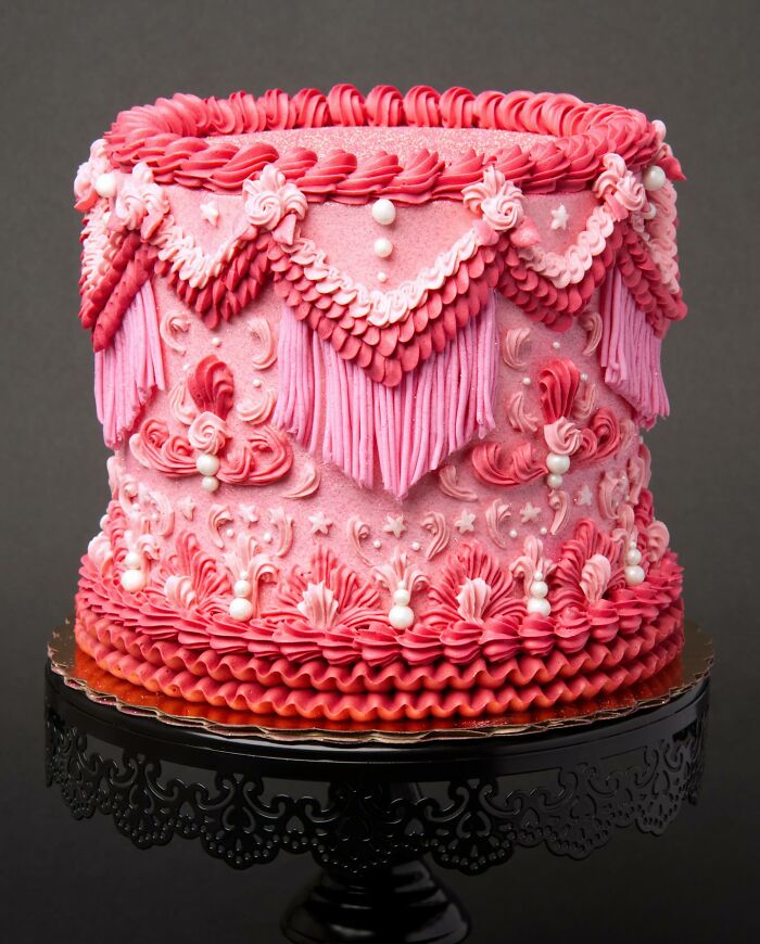 A visually stunning pink cake with intricate icing decorations on a black ornate stand.