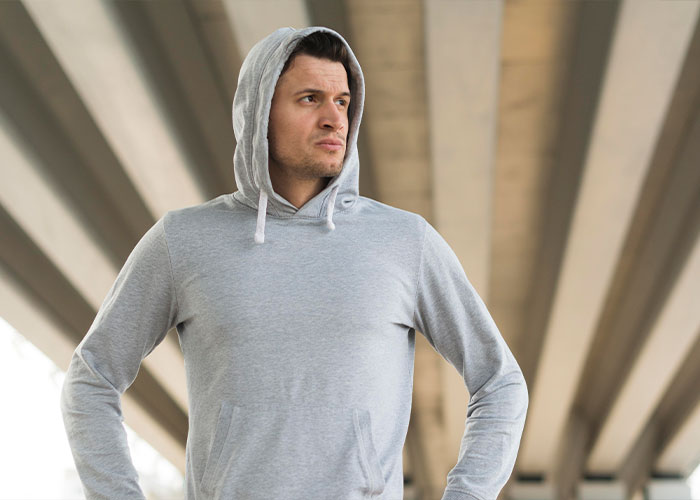 Man in gray hoodie standing confidently under a bridge, highlighting traits less attractive to some men.