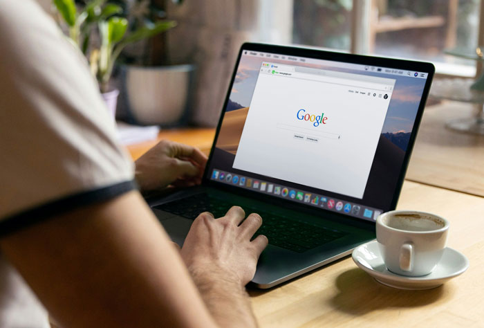Person using internet hacks with a laptop, Google search open, cup of coffee beside, enhancing online productivity.
