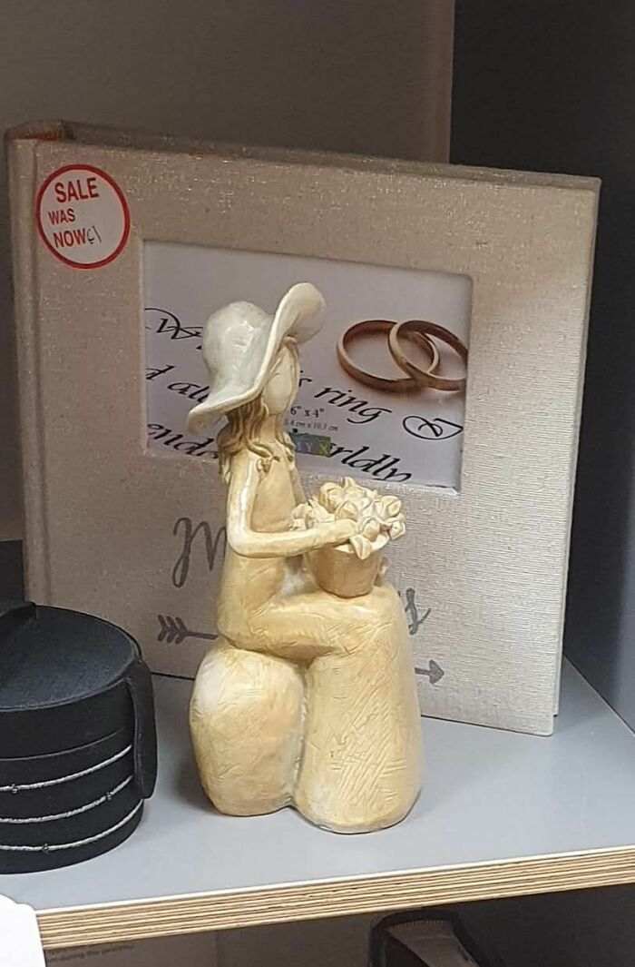 Clay sculpture of a woman with a hat and flowers, placed near a framed sale sign—secondhand shop treasure.