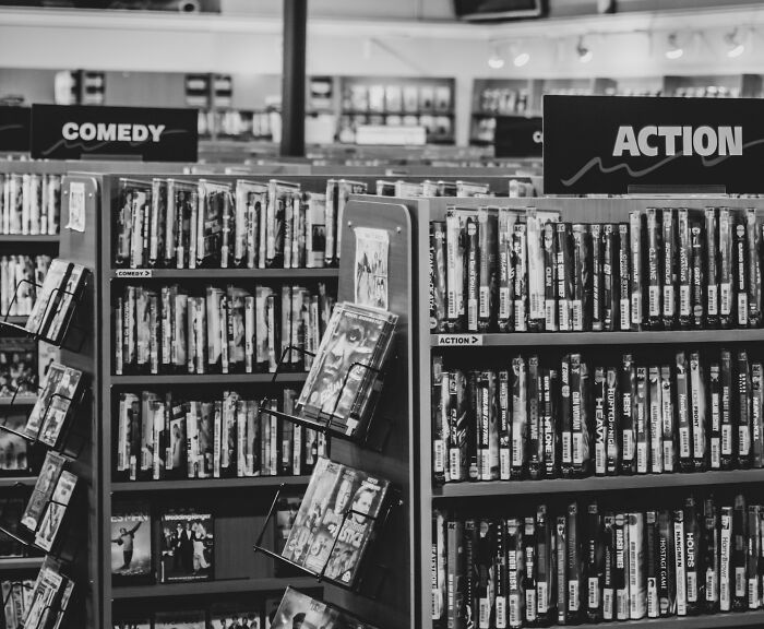 Video rental store shelves filled with DVDs in the comedy and action sections; a nostalgic scene from 30 years ago.