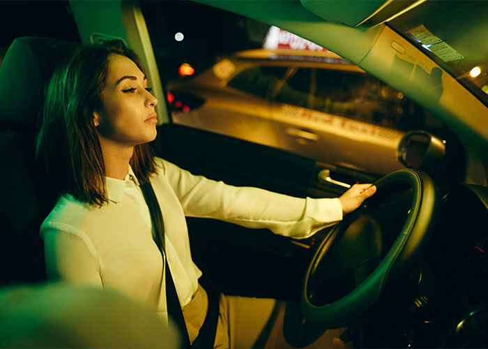 A woman in a car at night, eyes closed, illustrating unrealistic movie scenes that disrupt storytelling.
