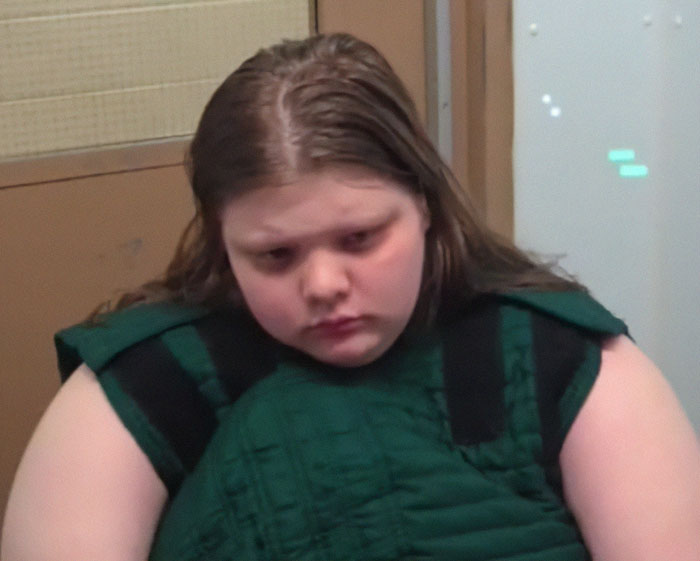 Teen involved in a violent family dispute, looking down in a courtroom setting.