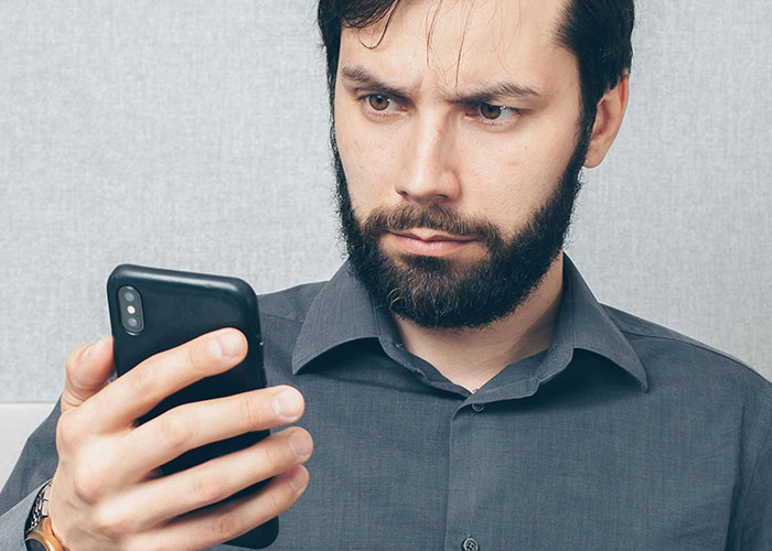 Man with a beard looking shocked at his phone, illustrating heartbroken people realizing their significant others were cheating.