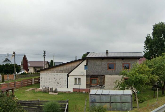 Unfinished multi-material real estate property with garden and greenhouse under a cloudy sky in a rural area.