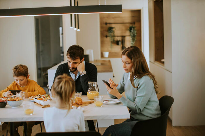 Family having breakfast, displaying bizarre house rules with unusual phone usage and distracted interactions.