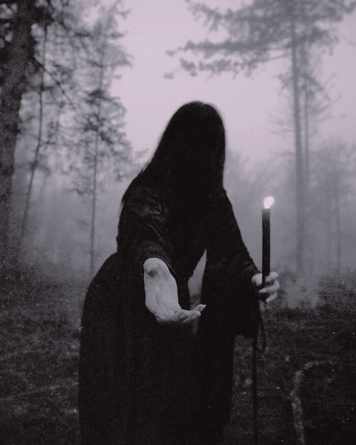 Dark escapism photography by Nona Limmen, figure with candle in misty forest.