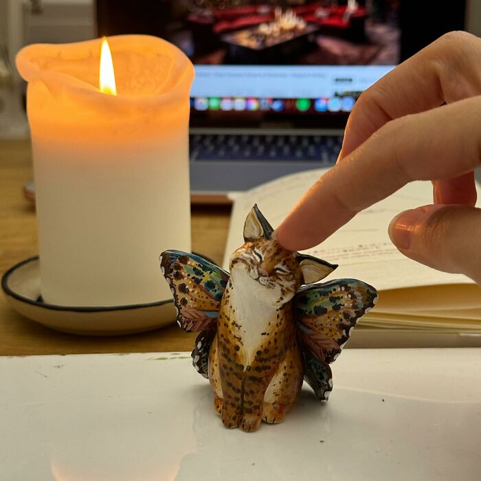 A hand touching a cute pocket-sized animal figurine with butterfly wings by a candle.