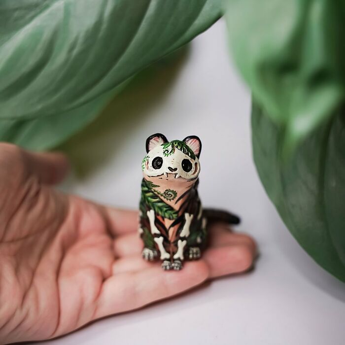 Hand holding a Vallavica pocket-sized animal figurine, surrounded by green leaves.