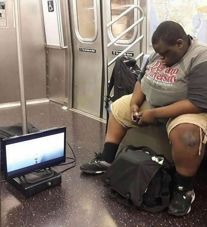 Man on subway plays video game with portable screen; random funny image shared on Instagram.