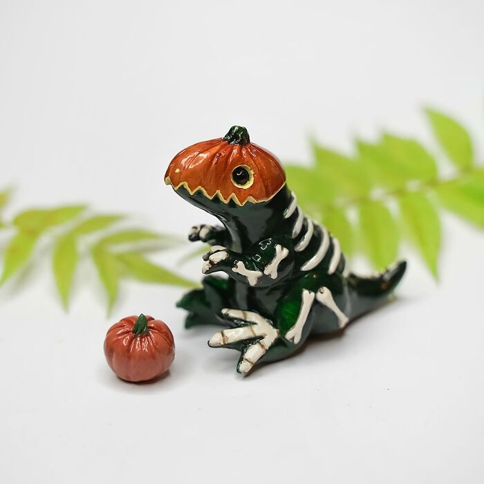 Pocket-sized animal figurine with a pumpkin head, crafted by Vallavica, next to a mini pumpkin and leafy background.