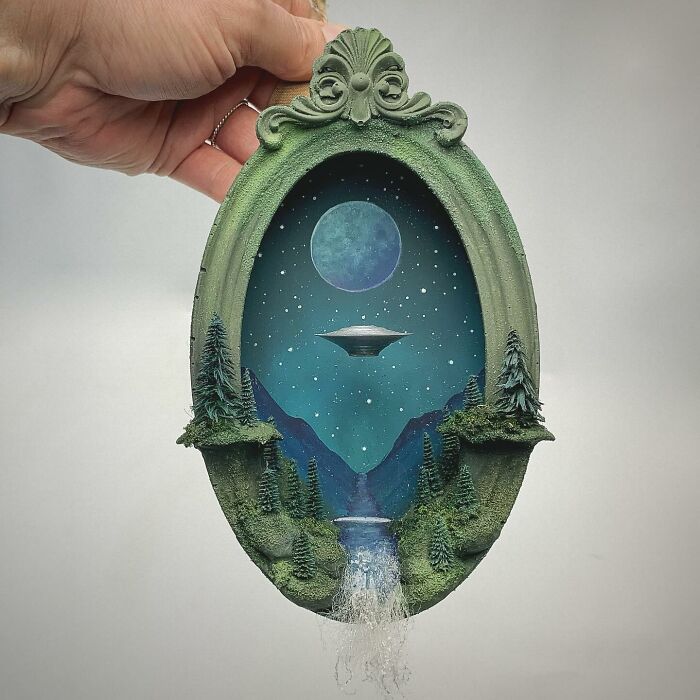 Alien-themed diorama by Caroline Dewison, featuring a UFO, moon, and lush landscape in an ornate frame.