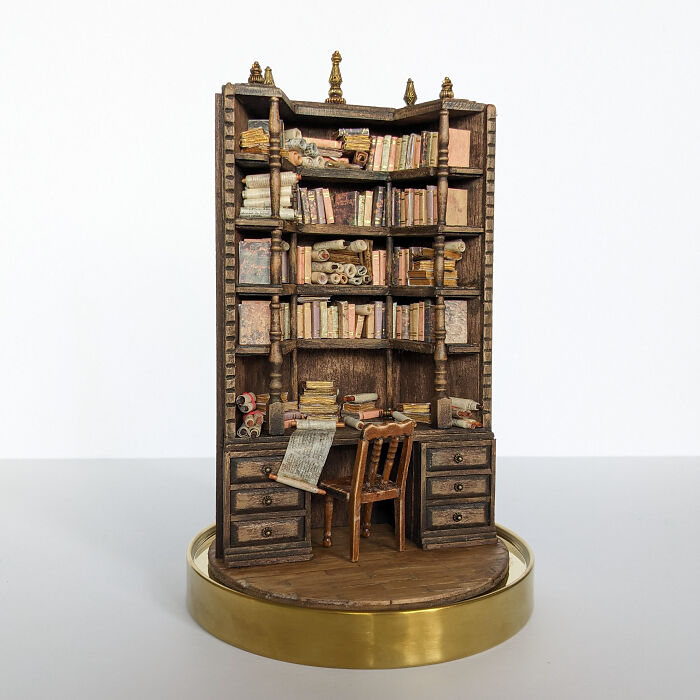 Miniature bookshelf with scrolls and books, featuring a tiny desk and chair, crafted by Tamar Cohen.