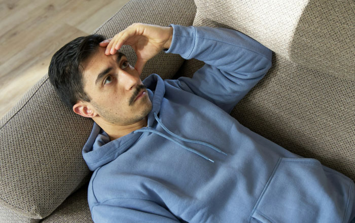Man in a blue hoodie lying on a couch, appearing thoughtful about family DNA results.