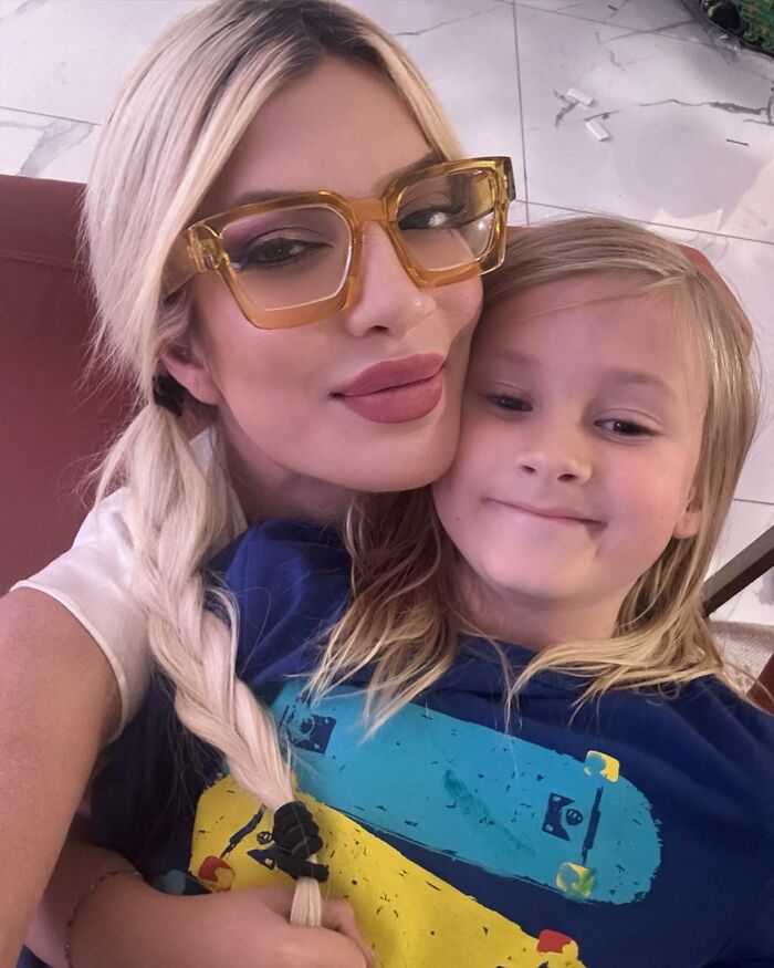 Woman with blonde braided hair and yellow glasses taking a close selfie with a smiling child, showcasing celebrity encounters.