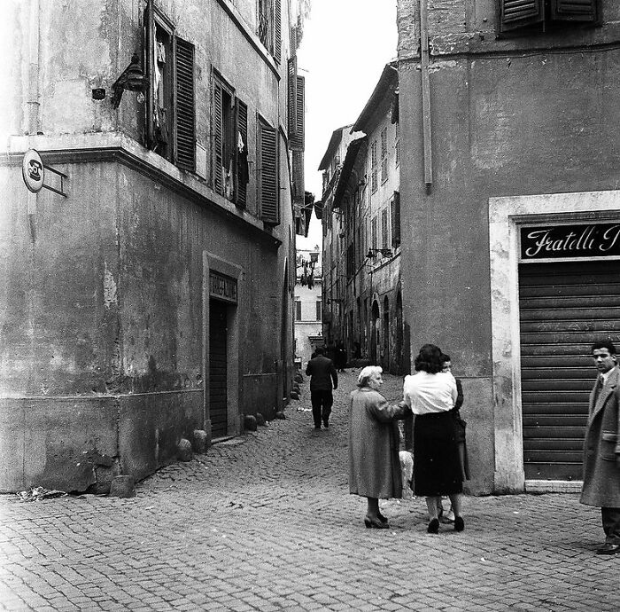 Black and white photo of a European street scene showing daily life in Europe 100 years ago with people walking.