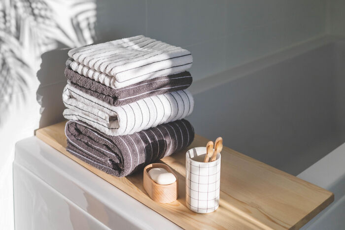 Stack of neatly folded towels on a wooden bath tray next to toothbrushes in a holder, representing house rules aesthetics.