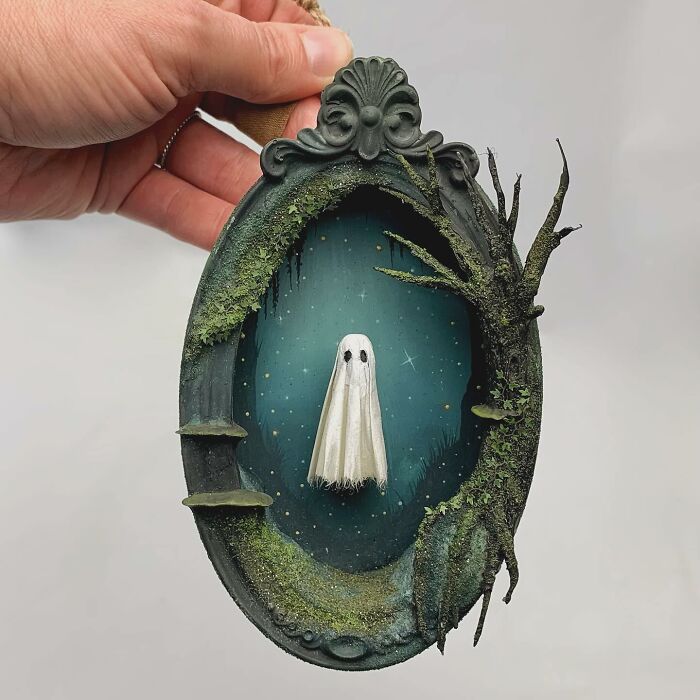 Ghost diorama by Caroline Dewison, featuring a ghostly figure in an ornate oval frame with moss and tree branches.