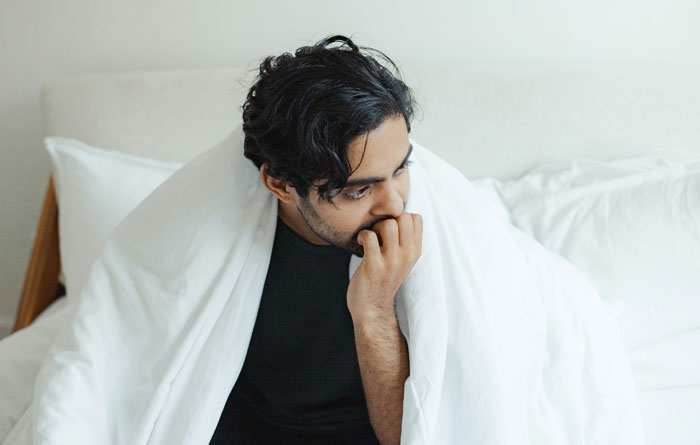 Man looking contemplative on bed, wrapped in a white blanket, reflecting on unexpected family DNA results.