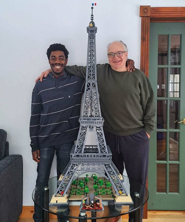 Two men smiling and posing with a detailed miniature Eiffel Tower model, capturing pure and uplifting moments.