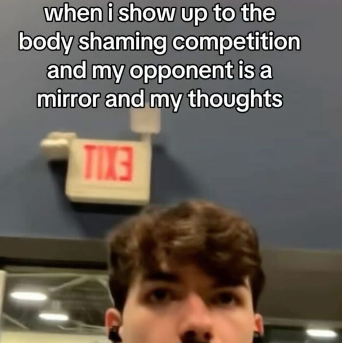 Man in a gym with text about a relatable body shaming meme, looking up at an exit sign.