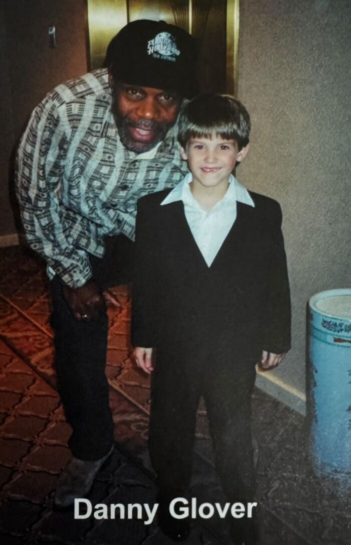 Childhood photo with a celebrity, featuring a young boy in a suit and a man wearing a hat, smiling together indoors.