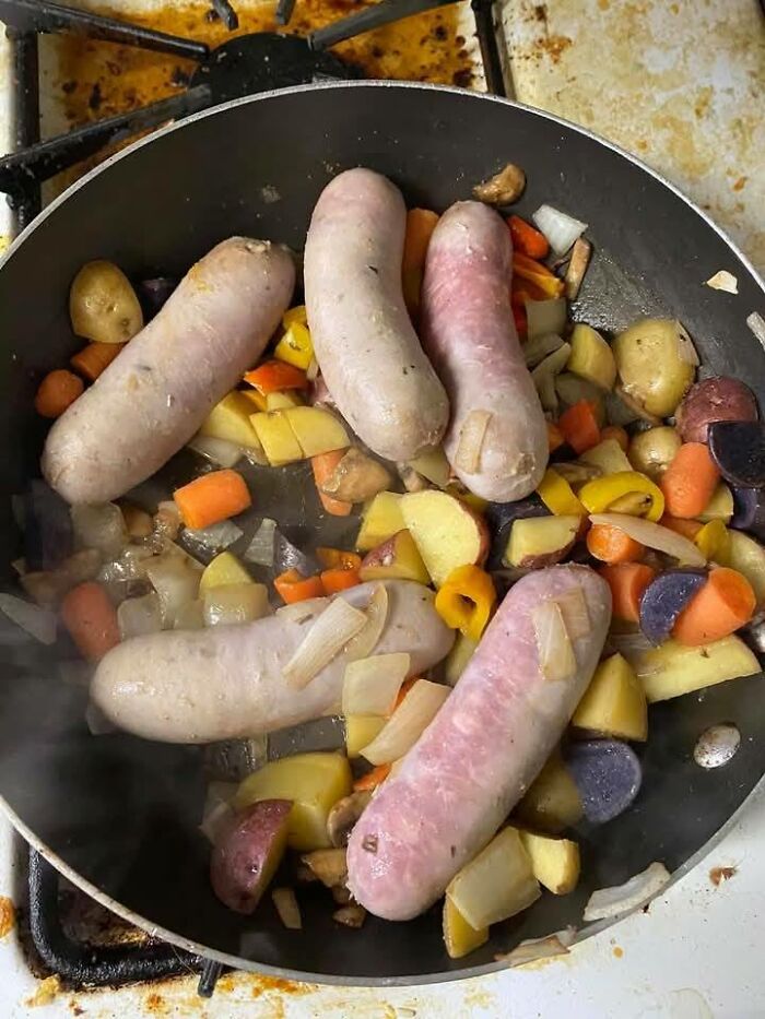 Unappetizing potluck dish with sausages and unseasoned vegetables in a frying pan.