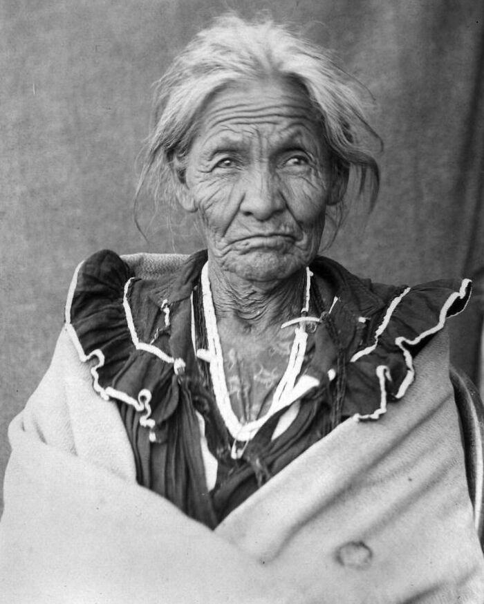 Elderly Native American woman wrapped in a blanket, showcasing the real lives of Native Americans a century ago.