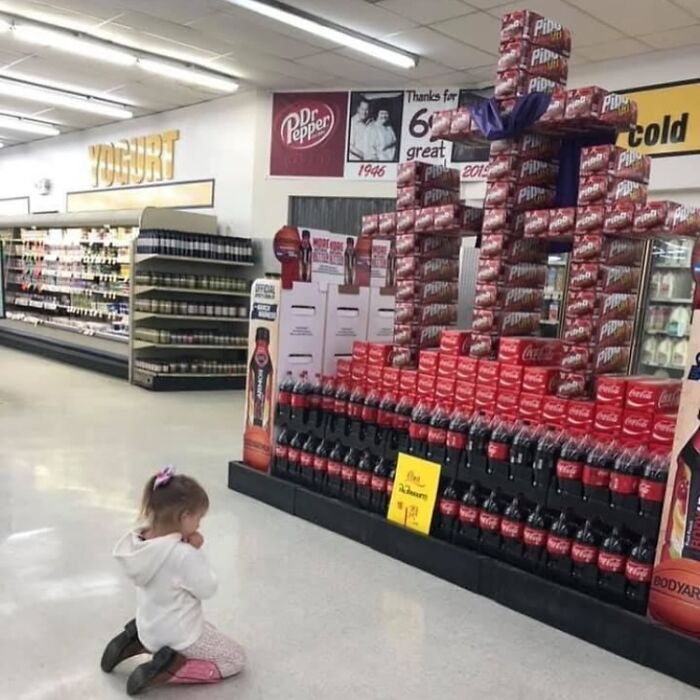 A child kneeling in front of a soda display shaped like a castle in a grocery store, capturing random funny moment.