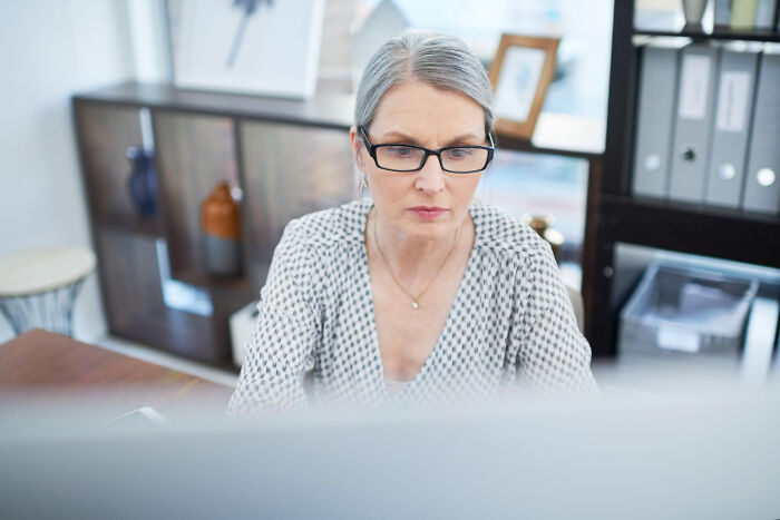 Professional woman at desk, wearing glasses, engaged in work drama with intense focus.